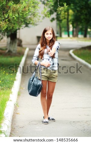 Schoolgirl Outdoor with book bag shows thumb up okey. Back to School
