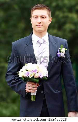 young groom waiting for bride in the yard over green background holding flowers