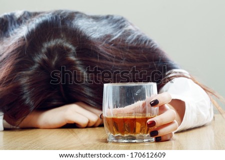 Drunk woman holding an alcoholic drink and sleeping with her head on the table (Focused on the drink