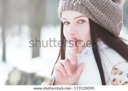 Portrait of beautiful woman wearing winter clothes gesturing to be quiet over snowfall background