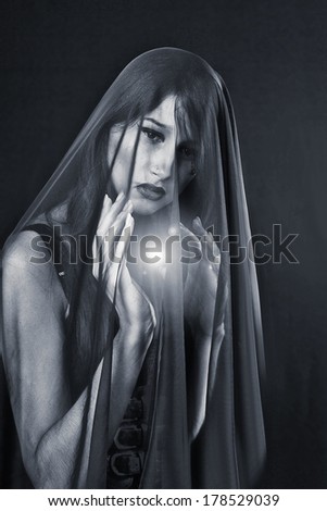 beautiful sad woman covered by transparent fabric on dark background widow