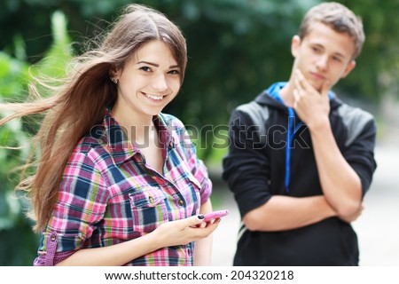 Young couple flirting in the green park. Girl holding phone going to call to boy