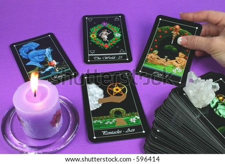 The hand of a reader laying out a tarot reading (with candle and deck in foreground)