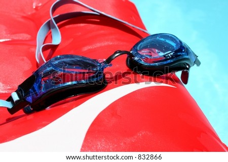 Blue swimming goggles on red boogie board, floating in swimming pool