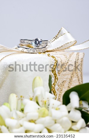 close of up engagement and wedding rings on gift box with orange blossom flowers in foreground