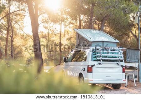 Campervan caravan vehicle for van life holiday on mobile home camper mobile motor home. Golden sunshine sneaking through sparse trees of camping. Roof of campervan is covered in colourful sunshine
