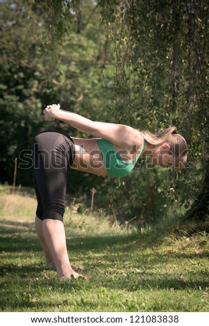 A blonde women make Yoga unter a tree in green grass