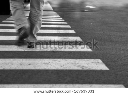 A  black and white picture of a man walking on a crosswalk. picture has grain .