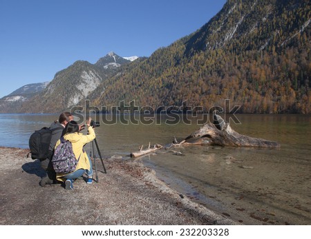 Couple is taking a picture of a trunk in the water.Picture is made on a sunny autumn day .The driftwood is laying near the riverside.
