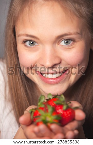 Close up Cheerful Pretty Girl Holding Fresh Red Strawberries with Toothy Smile on her Face and Looking at the Camera.