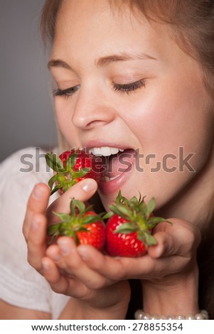 Close up Attractive Young Woman Biting Fresh Red Strawberries in Sexy Way with Mouth Open on a Gray Background.