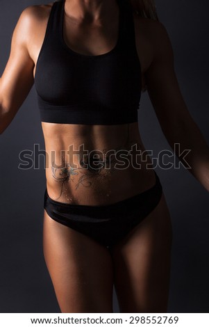 Picture of a Women with a wet boddy and a tattooed belly. Muscular fitness women with black underwear.