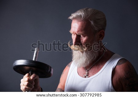 Senior man with long white beard and a white t-shirt makes a workout with a dumbbell.
