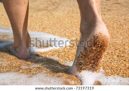 Barefoot feet walking in surf on sand coast