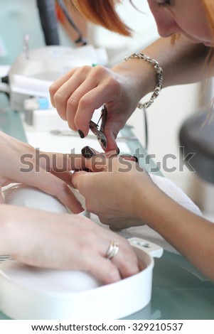 The manicurist holds hands of the client in beauty salon on desktop for manicure with nail polishes, napkins, creams and lighting instruments