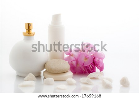 Spa cosmetics, creams with pink flower, soap and pebbles on white background