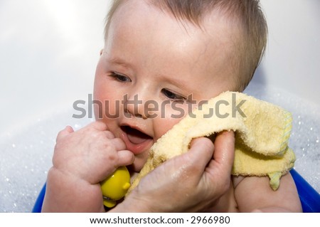 A baby having his face washed in the bath