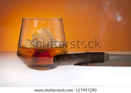 Tumbler with Whiskey on the rocks and smoking cigar