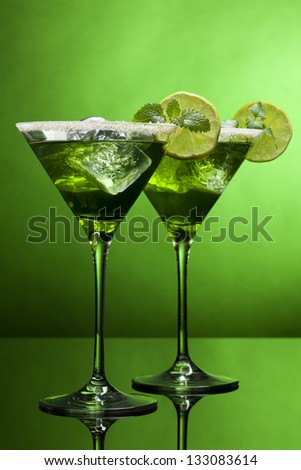 Two martini glasses with green cocktails in green light