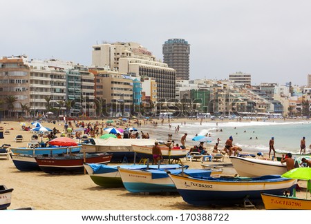 Las Palmas, Spain - July 1, 2011: Spanish families and tourists enjoying their day at the crowded beach of Las Canteras, the second longest city beach in the world. Colorful fisherboats on the sand.