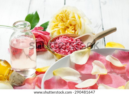 Rose petals in bowl of water, bath salt and bottle with oil, flowers in background