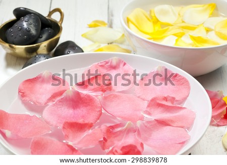 bowls with yellow and pink rose petals floating on water and massage stones