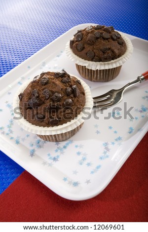 two chocolate muffins on white plate, garnished with little stars, on blue and red surfaces