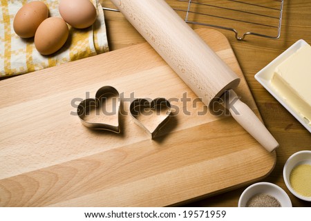 heart shaped cookie cutters on wooden board, rolling pin and baking ingredients