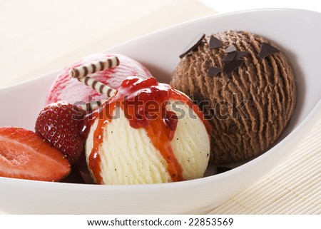 three balls of ice-cream - chocolate, strawberry, vanilla, in white bowl, garnished with strawberries, chocolate and red sauce