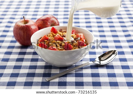 milk being poured into bowl of cereal flakes with fresh fruit