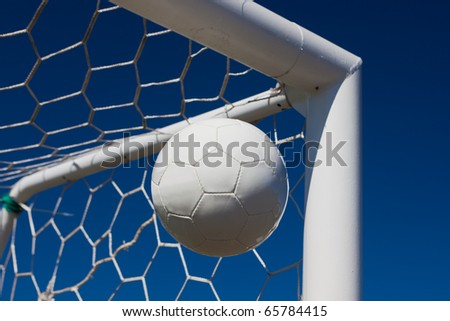 Close-up of a soccer ball (football) going into the top corner of the goal with a blue sky background.