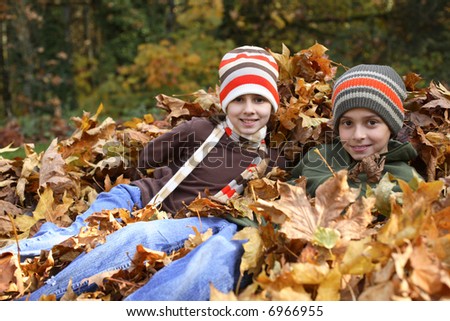 Young boy and girl sitting in pile of leaves
