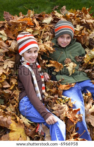 Young boy and girl sitting in pile of leaves