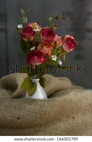 Still life with rose flower in white vase on sackcloth