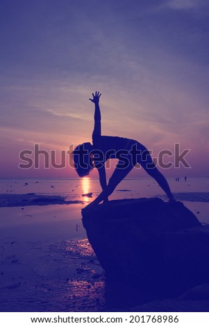 Silhouette vintage  yoga girl by the beach at sunrise Triangle  pose on rock