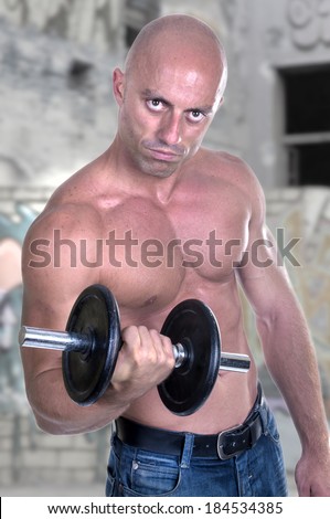 Muscular guy doing exercises with dumbbell outdoor