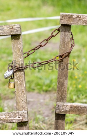 Wooden gate in a meadow is secured with a chain and lock / security / lock