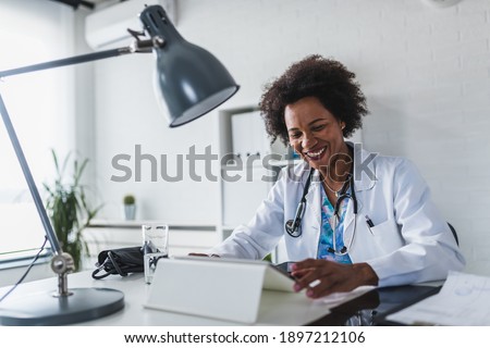 African American woman doctor working at her office online using portable inormation device. Telemedicine services. Primary care consultations, psychotherapy, emergency services. 