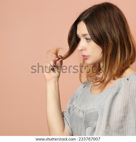 Damaged hair,  Woman with worried look on her face looking at the tips of her dry, damaged hair
