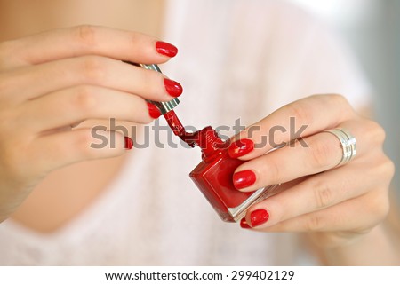 Woman applying red nail polish on her fingers - focus on the brush.
