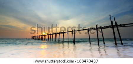Waves crashing onto the shore and broken wood bridge on sea at sunset