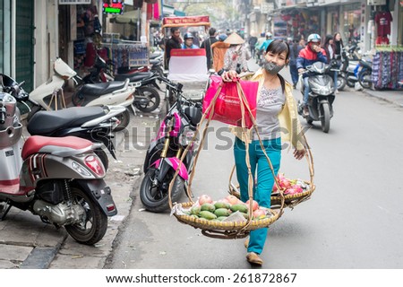 HANOI, VIETNAM   FEBRUARY 10: Fruit seller walks with a carrying pole in the old quarter on February 10, 2015 in Hanoi. The 36 old streets and guilds of the old quarter are a major tourist attraction.