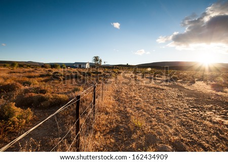 Sun sets over a semi arid desert as a farm fence runs throughout this image. This image contains sunfalre and a sunburst