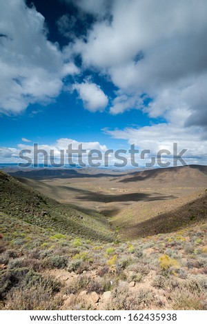A portrait view of a semi arid landscape with clouds casting a shadow