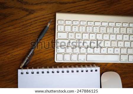 An Arial view of an  iMac wireless keyboard, mouse, pen, and desk pad on an oak wood desk