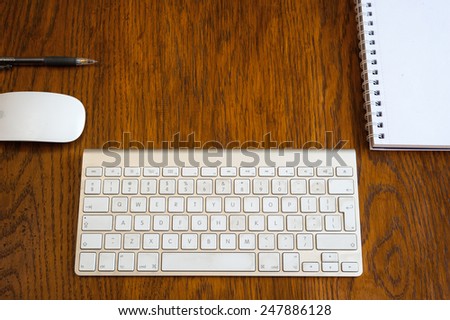 An Arial view of an  iMac wireless keyboard, mouse, pen, and desk pad on an oak wood desk