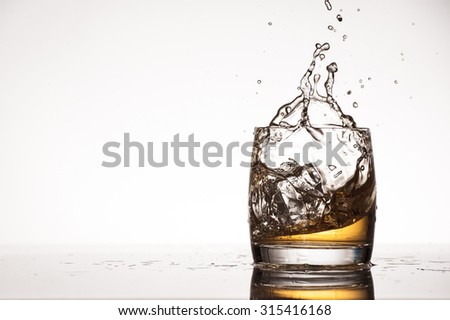 Ice splashing into a tumbler filled with whiskey/brandy on a white background photographed in studio