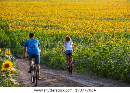Two happy teen cyclist in sunflower field riding bicycle