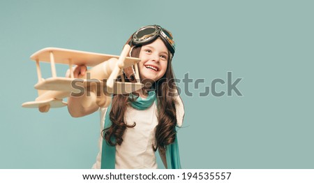 Beautiful smiling child (kid, girl) in helmet on a blue background playing with a plane. Vintage pilot (aviator) concept