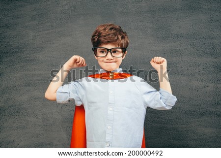 Cheerful smiling little kid (boy) against  chalkboard raised his hands up.  School and superhero concept